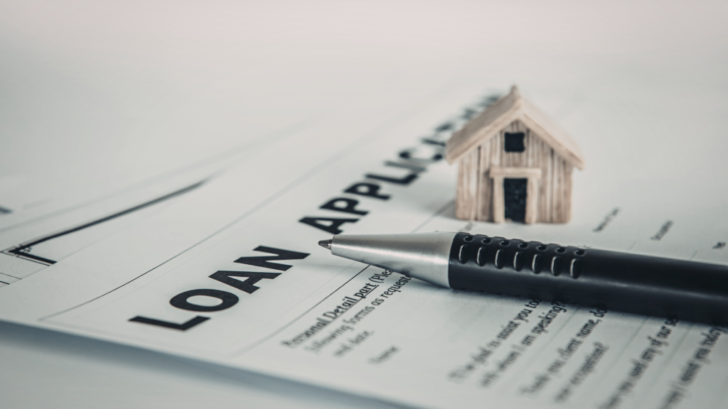 Home loan application with a pen and a small wooden replica of a house.